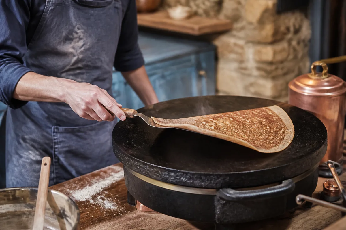 Crêpier retournant une galette à la spatule sur une plaque professionnelle